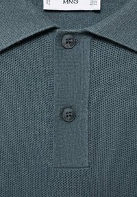 Dark green polo shirt made of textured fabric, featuring a collar, two black buttons, and a woven pattern.