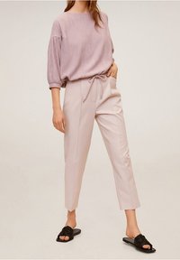 Lichtroze gebreide trui met korte, opgeblazen mouwen gecombineerd met lichtbeige op maat gemaakte broek en zwarte platte sandaal slippers.