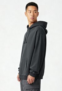 Felpa oversize grigia scura con cappuccio regolabile e tasca a marsupio. Presenta polsini e orlo a costine. Realizzata in materiale morbido e strutturato.