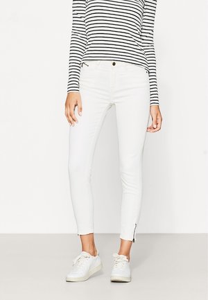 Jeans blancos ajustados con detalle de cremallera en los tobillos, combinados con una camiseta de manga larga a rayas blancas y negras. Tela suave, mezcla de algodón.