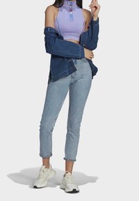 Ljuslila kort sporttopp med dragkedja, lagd under en blå denimjacka. Ljust blå skinny jeans och vita sneakers fulländar outfiten.