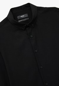 Sort slim-fit skjorte med knaplukning lavet af tekstureret stof. Har en krave, seks sorte knapper og et mærke med brand- og størrelsesoplysninger.