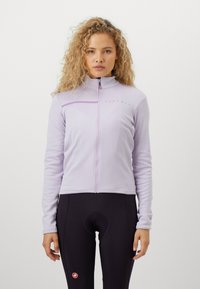 Svetlestrofialová dlhá bunda na zips z mäkkého materiálu, vybavená vyšitým logom a vysokým golierom, v kombinácii s čiernymi cyklistickými šortkami.