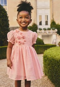 Ružové ľanové šaty s krátkymi nafúknutými rukávmi, s nariasenou sukňou a kvetinovými aplikáciami na živôtiku. Hladká textúra a ľahký dizajn.