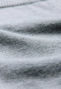 Tela de color gris claro con textura suave, presenta un patrón acanalado y un ligero brillo, mostrando pliegues y sutiles variaciones en el tono.