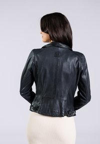 Schwarze Lederjacke mit tailliertem Design, versehen mit einem Reverskragen, vertikalen Nähten und Schnallenakzenten an der Taille. Glatte, sichtbare Textur.