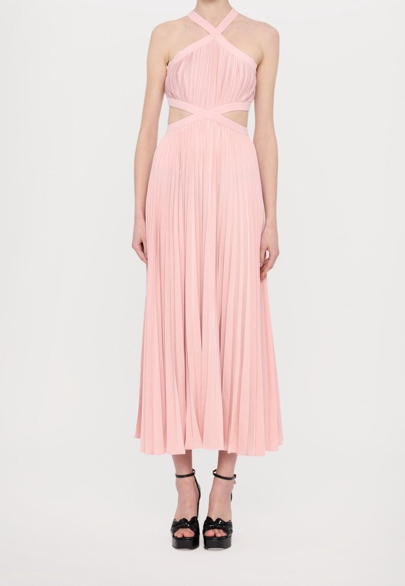 Robe midi plissée en rose doux, avec un col halter croisé et des découpes à la taille ; associée à des chaussures à plateforme noires.