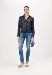 Marineblauw kantshirt met lange mouwen, knoopsluiting, scalloped zoom, gecombineerd met lichtblauwe skinny jeans en beige hoge hakken.