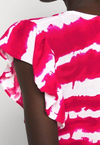 Krótki rękaw bluzki w biało-różowy wzór tie-dye, z falbaniastymi rękawami i miękką fakturą.