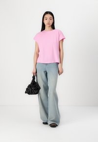 Rožinė trumpa rankovė t-shirt su laisvu siluetu, derinama su šviesiai mėlynomis platėjančiomis džinsomis ir juoda gėlių rankine. Lygi medžiaga ir paprastas dizainas.