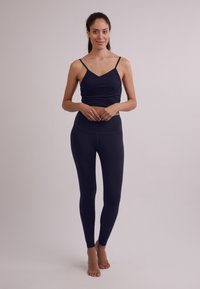 Completo sportivo a due pezzi in blu navy, composto da un top aderente con spalline sottili e leggings a vita alta. Texture liscia in tutto il capo.