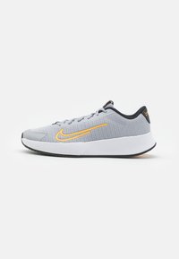 Scarpa sportiva grigia chiara con una tomaia in mesh texturizzato e suola in gomma bianca. Presenta un logo Nike giallo e dettagli neri sul tallone.