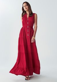 Červená kockovaná maxi šaty s gombíkmi na prednej strane, bez rukávov, s nastaviteľným opaskom a rozšírenou sukňou. Hladká textúra, uvoľnený strih.