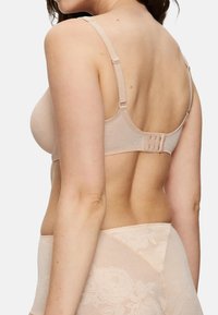 Lichtbeige bh met een bloemenkant overlay, verstelbare bandjes en een haak-en-oogsluiting aan de achterkant. Vlotte textuur en naadloos ontwerp.