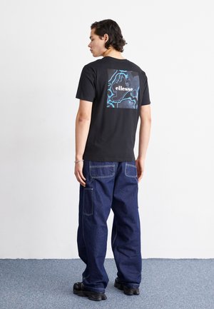 Schwarzes Baumwoll-T-Shirt mit einem Grafikdruck auf der Rückseite in Blau und Weiß, kombiniert mit dunkelblauen Denim-Cargohosen mit großen Taschen.