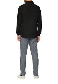 Schwarzes Langarmshirt mit Knopfmanschetten, kombiniert mit hellgrauen Chinos und weißen Sneakers, von hinten gezeigt.
