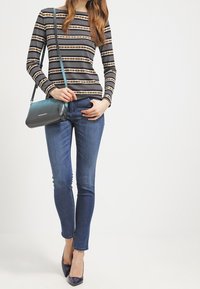 Gestreiftes Schwarz-Weiß-Oberteil mit langen Ärmeln, blaue Skinny-Jeans, türkisfarbene Umhängetasche und dunkelblaue High Heels. Glatter Stoff und taillierte Passform.