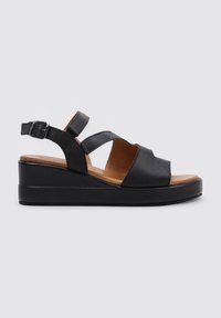 Sandalias de cuña de cuero negro con correa ajustable en el tobillo, diseño de punta descubierta y detalles recortados minimalistas. Plantilla marrón, suela texturizada.