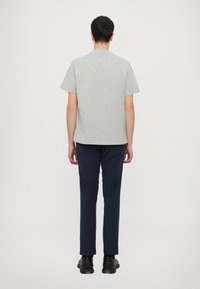 Szürke rövid ujjú póló, kerek nyakkal, elegáns tengerészkék nadrággal párosítva. A modell háttal áll, így a letisztult, díszítetlen design látható.