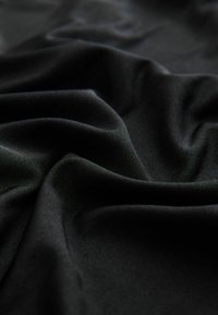 Zwarte stof met een gladde, matte textuur, met zachte draperingen en een subtiele glans, die zachte plooien en kreukels toont.