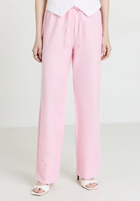 Pantalons larges de couleur rose clair avec une taille à cordon. Bordée d'une broderie florale à l'ourlet. Fabriqués en tissu doux et léger.