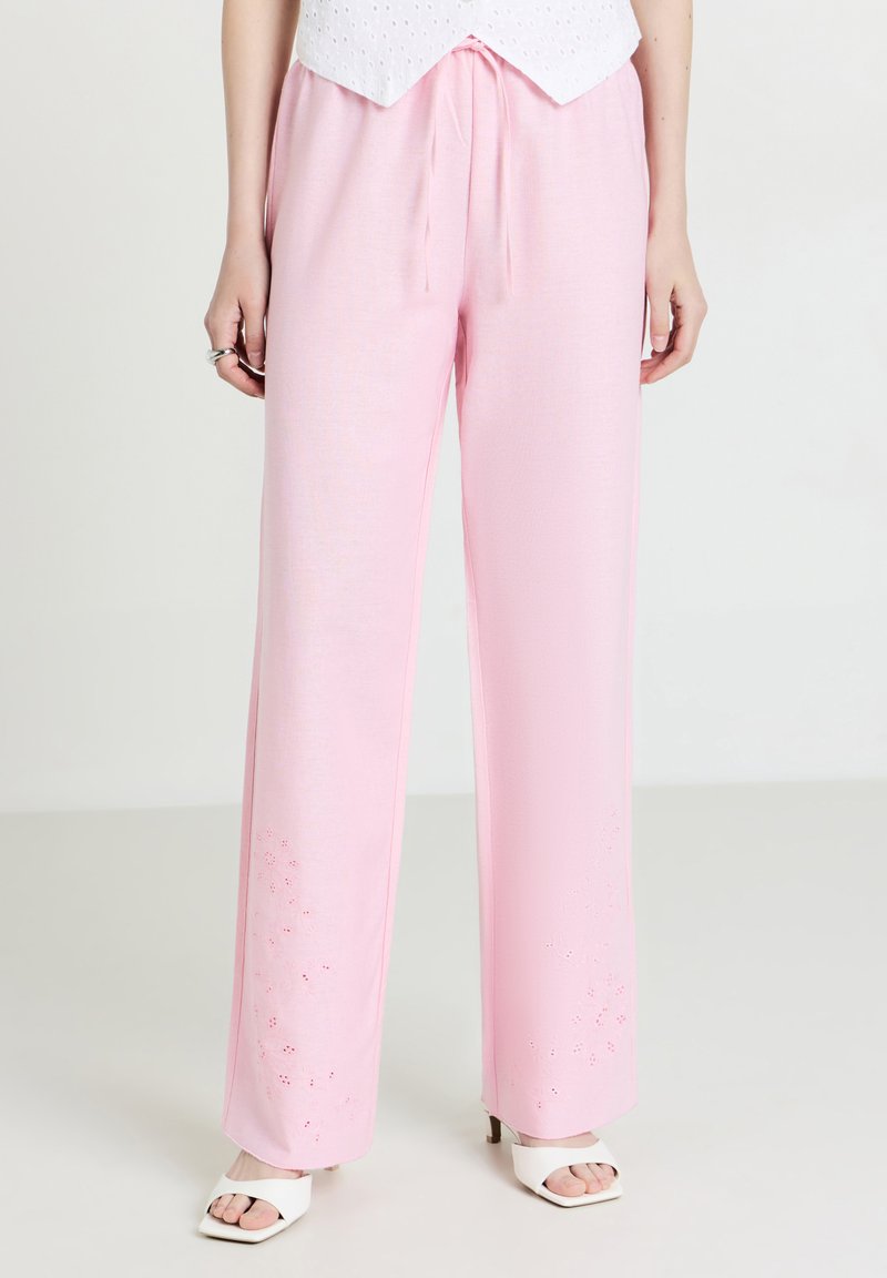 Pantalons larges de couleur rose clair avec une taille à cordon. Bordée d'une broderie florale à l'ourlet. Fabriqués en tissu doux et léger.