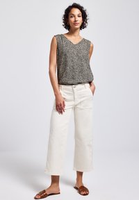 Top sin mangas negro y crema con escote en V y estampado de leopardo, combinado con pantalones de pierna ancha blancos de cintura alta y sandalias planas marrones.