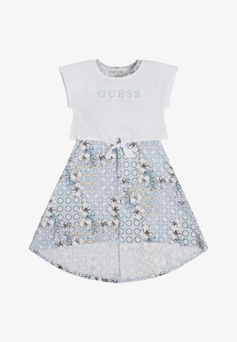 Vit bomullstopp med "GUESS LOS ANGELES"-logotyp. Blå kjol med blommönster, vit kant och knytning i midjan.