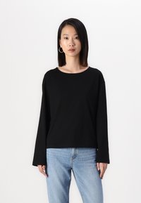 Svart langermet skjorte med rund hals, laget av mykt stoff. Kombinert med lyseblå denimjeans som har en avslappet passform.