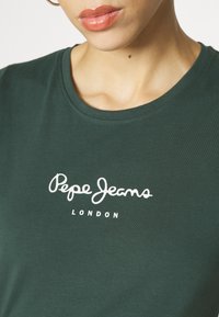 Tamsiai žalia medvilninė marškinėliai su apvaliu kaklu ir trumpomis rankovėmis, su balta logo, kurioje parašyta "Pepe Jeans LONDON" krūtinės srityje.