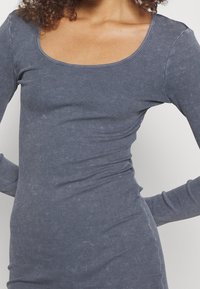 Långärmad topp i ribbat marinblått tyg, med en rundad halsringning och kroppsnära silhuett. Mjuk textur med subtil färgvariation.