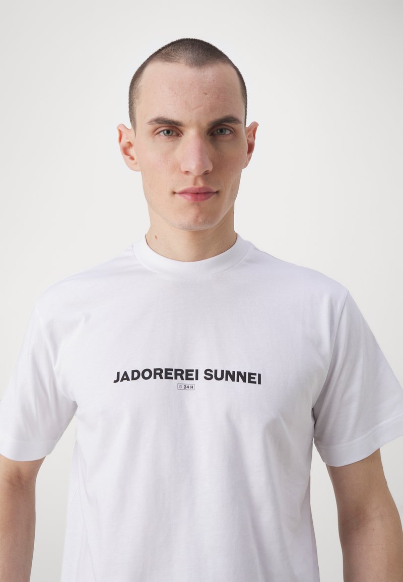 T-shirt bianca in cotone con stampa nera che presenta il testo "JADOREREI SUNNEI" al centro del petto, maniche corte e scollo rotondo.