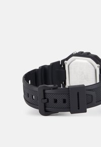 Black silicone watch strap with a textured surface, featuring a metal buckle and a rectangular silver case visible from the back.