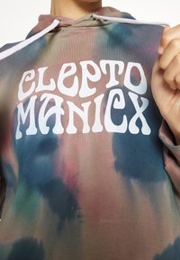 Mikina s tie-dye vzorem v tlumených zemních tónech růžové, modré a zelené. Na přední části se nachází bílý text s logem "CLEPTO MANIX". Materiál je směs bavlny.