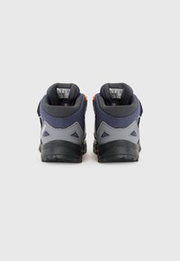 Vue arrière de chaussures de randonnée pour enfants avec une tige en maille bleu marine, des accents gris, un support au niveau du talon et une semelle en caoutchouc noir texturé. Détails orange.