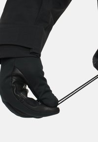 Schwarze Handschuhe mit einer strukturierten Lederhandfläche und einem Stoffkörper ziehen an zwei schwarzen Schnüren. Das Design ist enganliegend und ergonomisch.