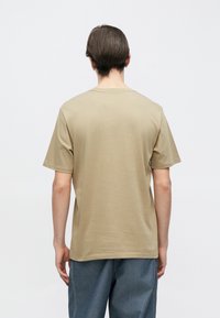 Μπεζ κοντομάνικη μπλούζα με στρογγυλή λαιμόκοψη. Ομαλή υφή, μονόχρωμη, απλός σχεδιασμός, χωρίς ορατά μοτίβα ή διακοσμητικά στοιχεία.