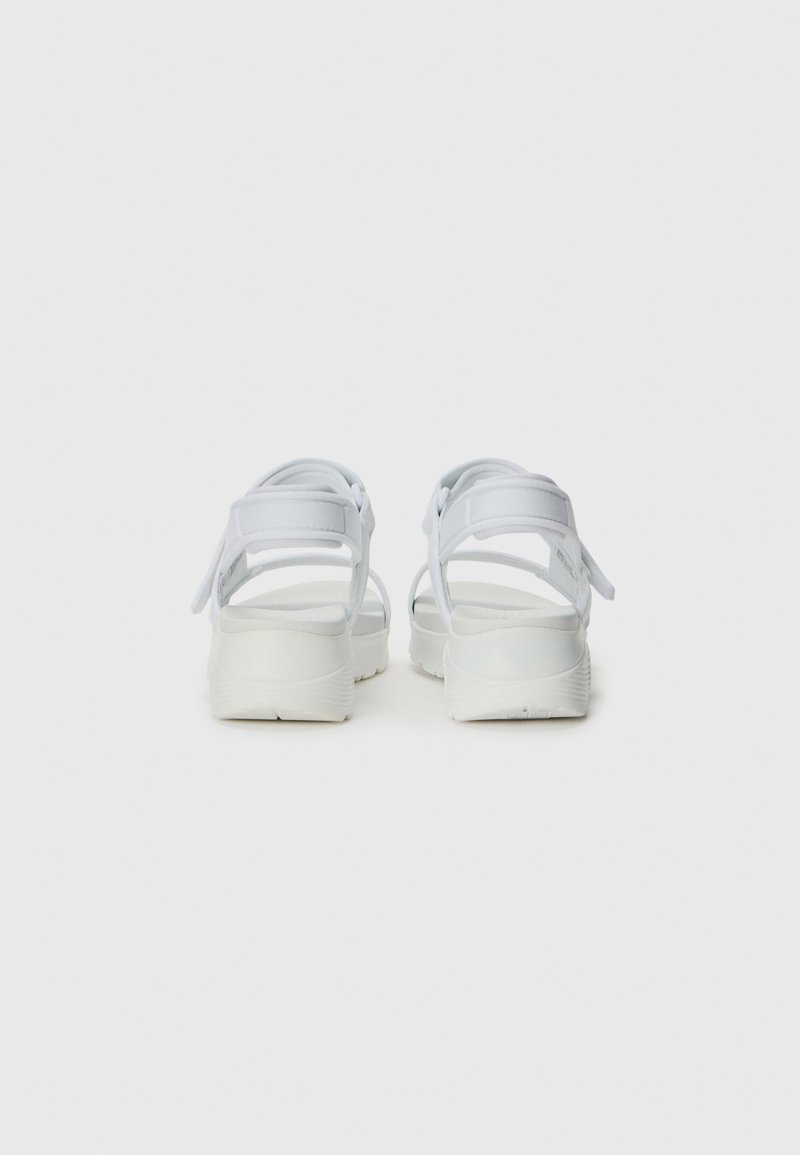 Sandalias blancas con múltiples correas ajustables; suela plana con superficie texturizada; diseño minimalista; material ligero.