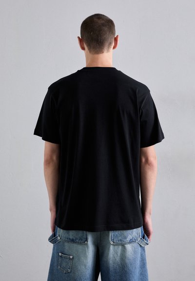 Tricou negru din bumbac, cu mâneci scurte, prezentat din spate, asortat cu șorturi din denim albastru decolorat, cu buzunare laterale.