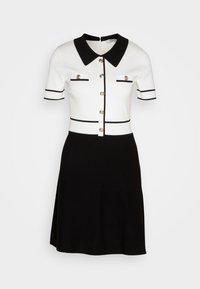 Haut blanc à manches courtes avec col noir, boutonnière devant, poches décoratives et bordure, associé à une jupe noire longueur genou.