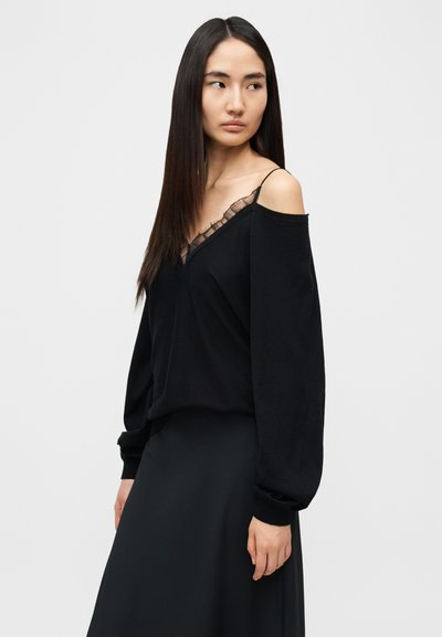 Haut noir épaules dénudées avec manches longues, doté d'un col en V orné de dentelle. Tissu doux avec une coupe décontractée.