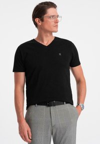 Sort v-hals t-shirt lavet af blødt stof med korte ærmer; har et subtilt logo på brystet. Bæres med grå ternede bukser.