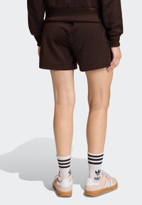 Brown athletic shorts with a smooth texture, paired with pink shoes and white socks featuring black stripes. Background is plain white.