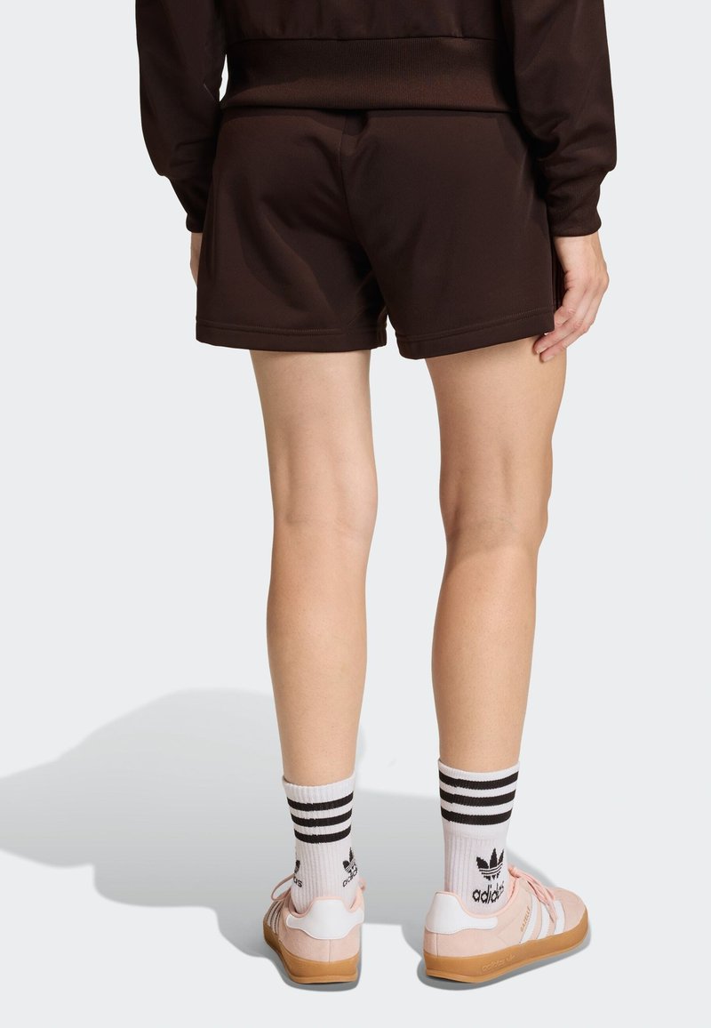 Brown athletic shorts with a smooth texture, paired with pink shoes and white socks featuring black stripes. Background is plain white.