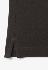 Tummanruskea teksturoitu kangas, jossa on pieni sivuleikkaus ja näkyvät ompeleet vaatekappaleen alaosassa.