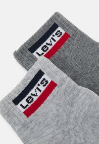 Graue Socken mit strukturiertem Rippenmuster, versehen mit einem eingewebten Levi's-Logo auf einem rechteckigen Patch in Marineblau, Weiß und Rot am Bund.