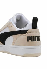 Sneaker beige e bianche con tomaia in suede e pelle, striscia laterale nera e logo "PUMA" nero ben in evidenza sul tallone. Suola in gomma.
