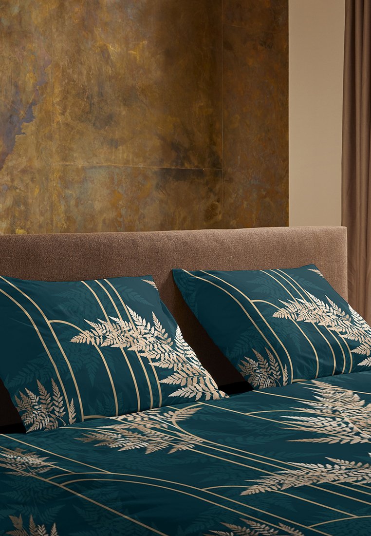 Ensemble de literie bleu canard avec un motif de feuilles de fougère en argent, comprenant des coussins décoratifs avec des accents linéaires, disposé sur un lit en beige capitonné.