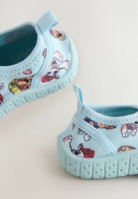 Chaussures pour tout-petits bleu clair avec des motifs de chiens de dessin animé, semelles flexibles texturées et languettes au talon sur un fond neutre.
