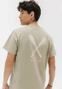 T-shirt in cotone verde oliva con scollo rotondo. Sul retro presenta due pagaie incrociate in rosa e menta con la scritta "elPulpo" sotto. Maniche corte, vestibilità standard.